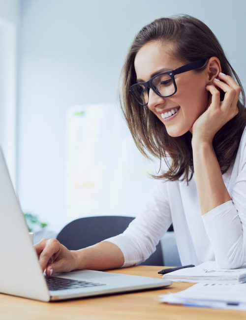 Portrait of beautiful cheerful young businesswoman working on laptop and laughing in home office